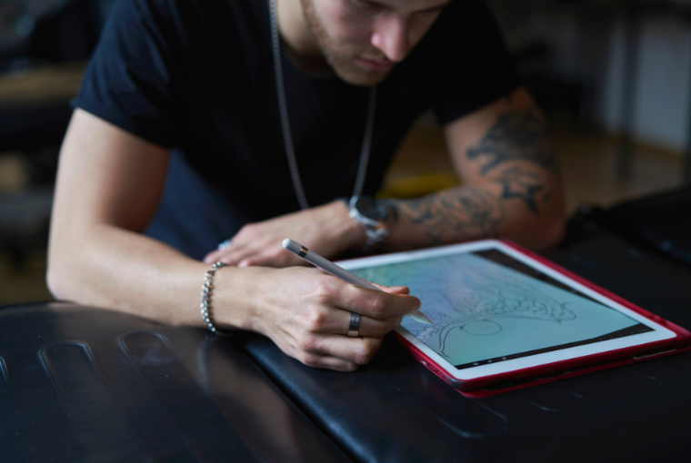 A tattoo artists sketches a design on a tablet