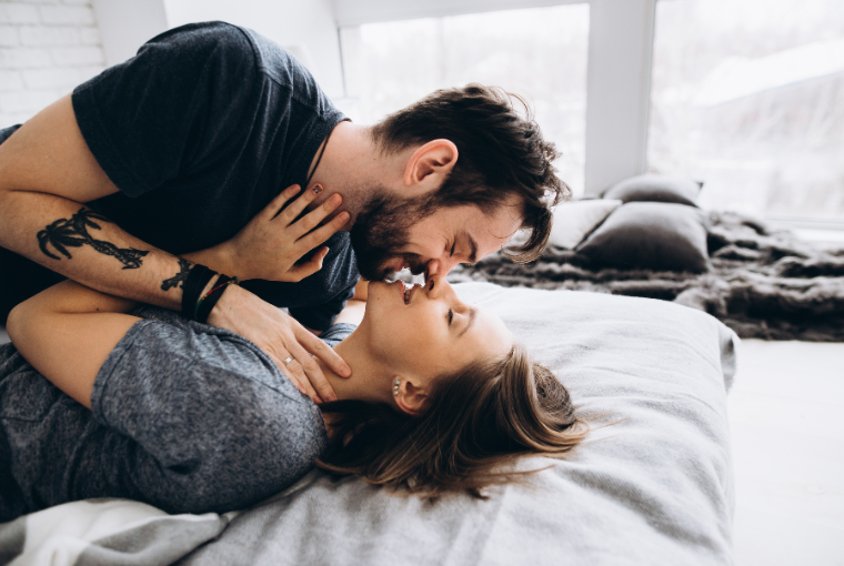 A couple with tattoos hugging on a bed