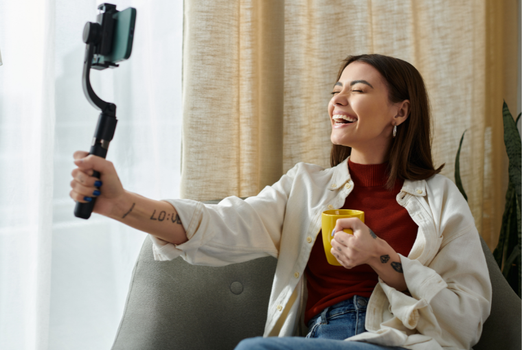 A young female influencer talks into her mobile with one hand and holds a yellow coffee cup in the other hand