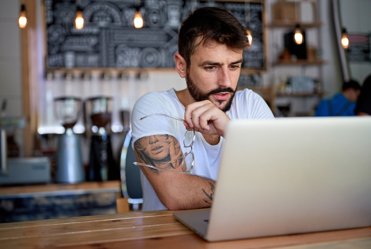 Tattoo professional on a coffee break looks thoughtfully at his laptop