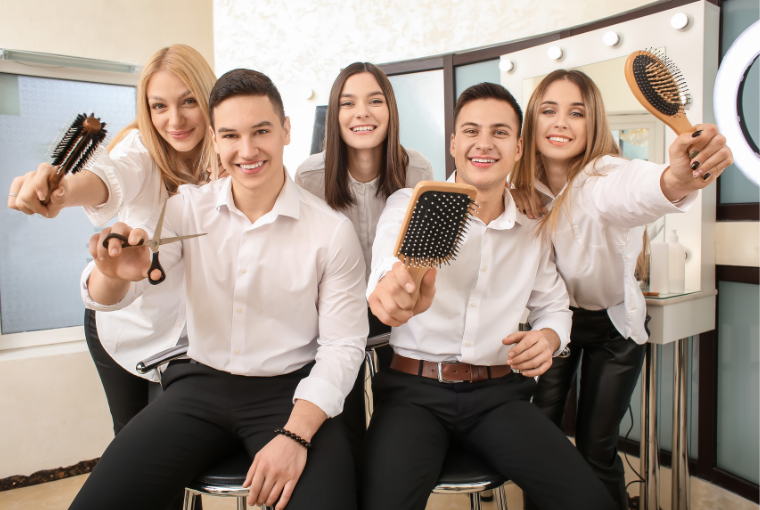 Group of young hair salon workers armed with brushes and scissors smiling and training together