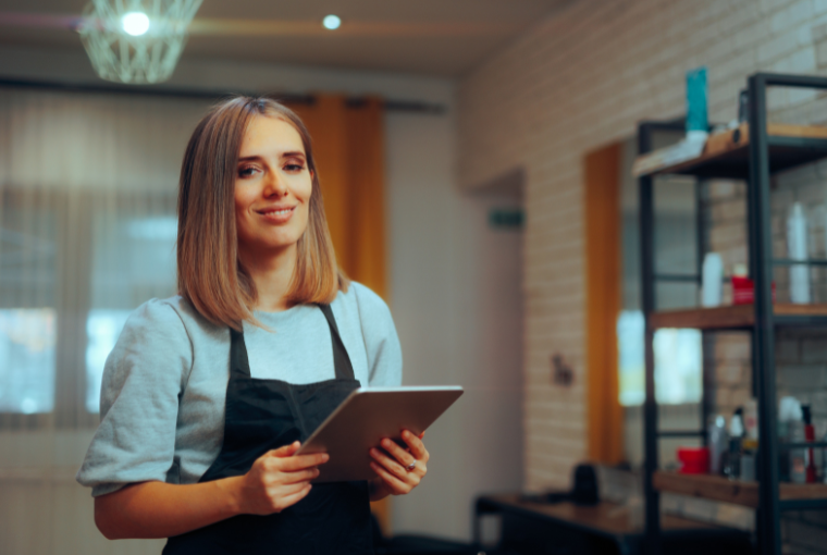 A hairdresser holding a tablet smiles at the camera 