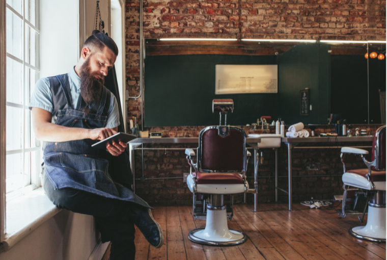 Barber taking a break and using Salon Management Software on a tablet