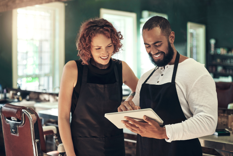 A female and male stylist using Salon Management Software on a white tablet and smiling