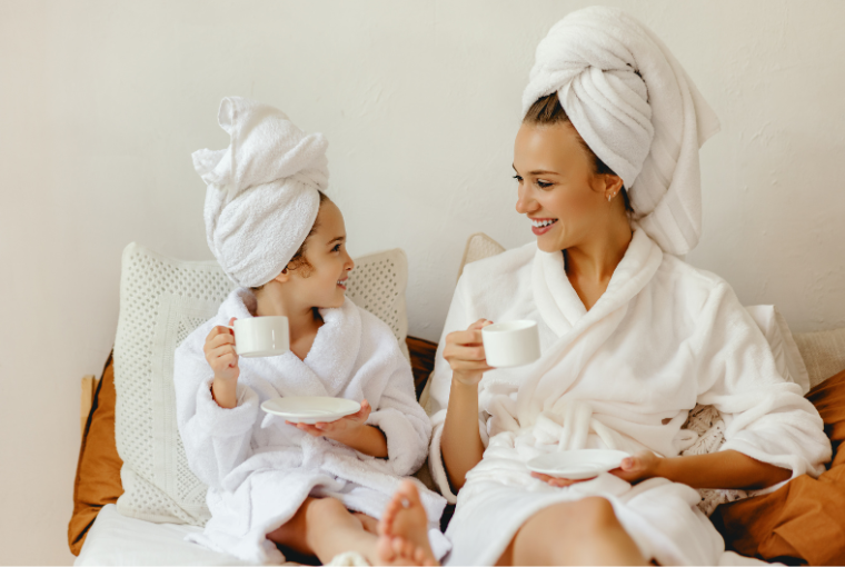 A young mom and daughter wearing gowns and fluffy towels on their heads enjoying some relaxation time