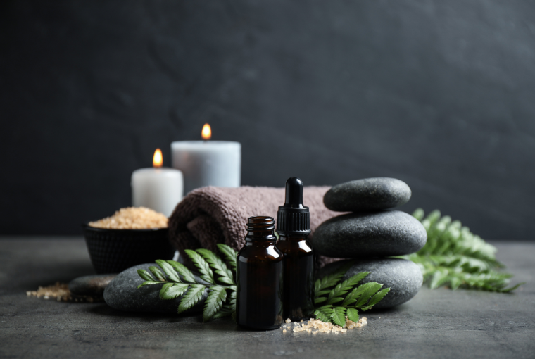 A calming spa scene with essential oils, hot stones, a fluffy towel, leafy green plants and two white candles burning